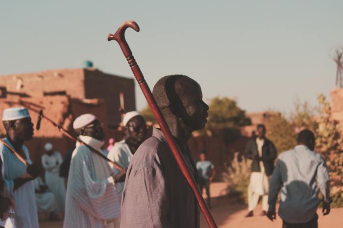 Man in black and white long sleeve shirt holding red stick in Sudan.